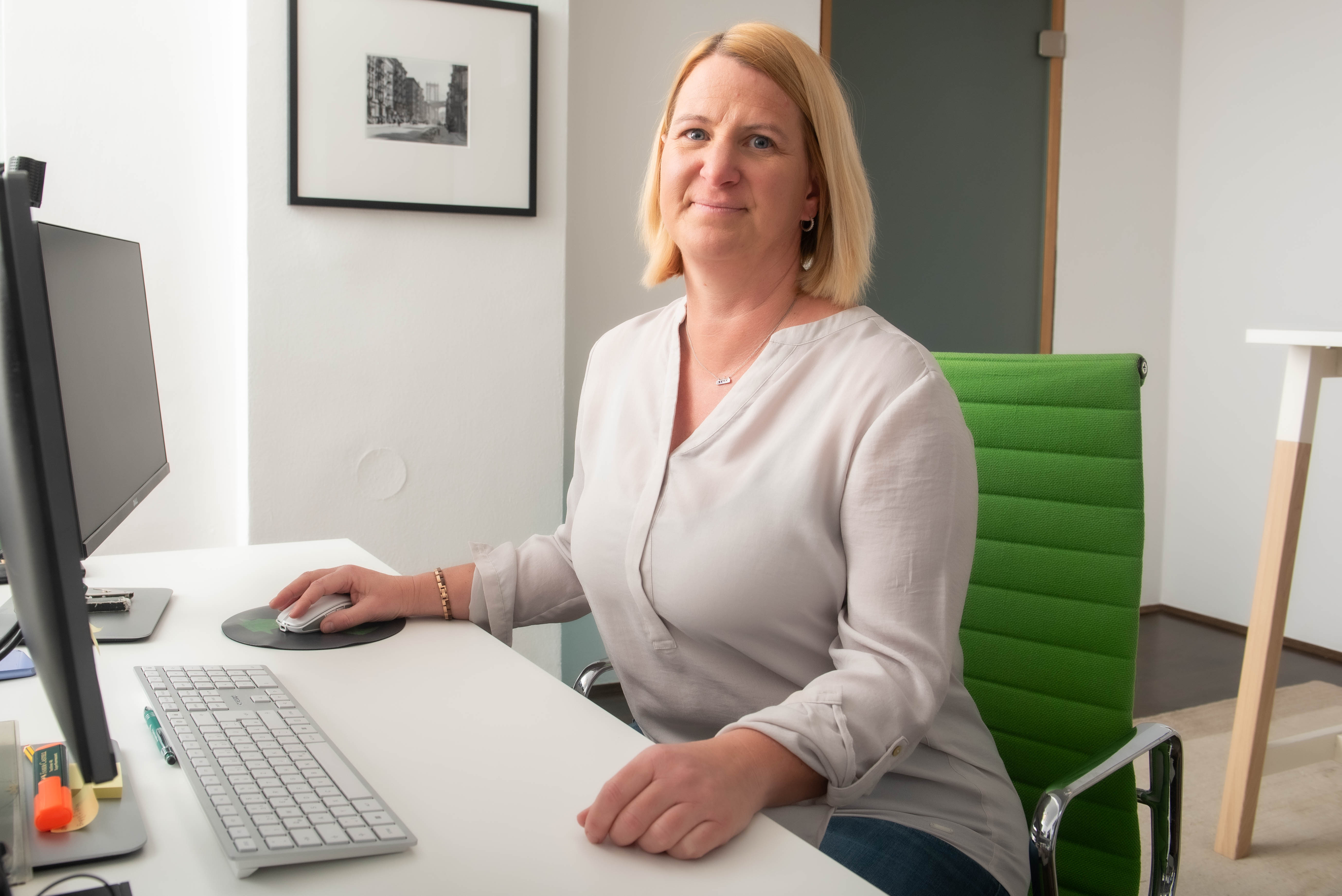 Christine Strauß an einem hellen Arbeitsplatz im Büro, sitzend vor Computer, Tastatur und Bildschirm.